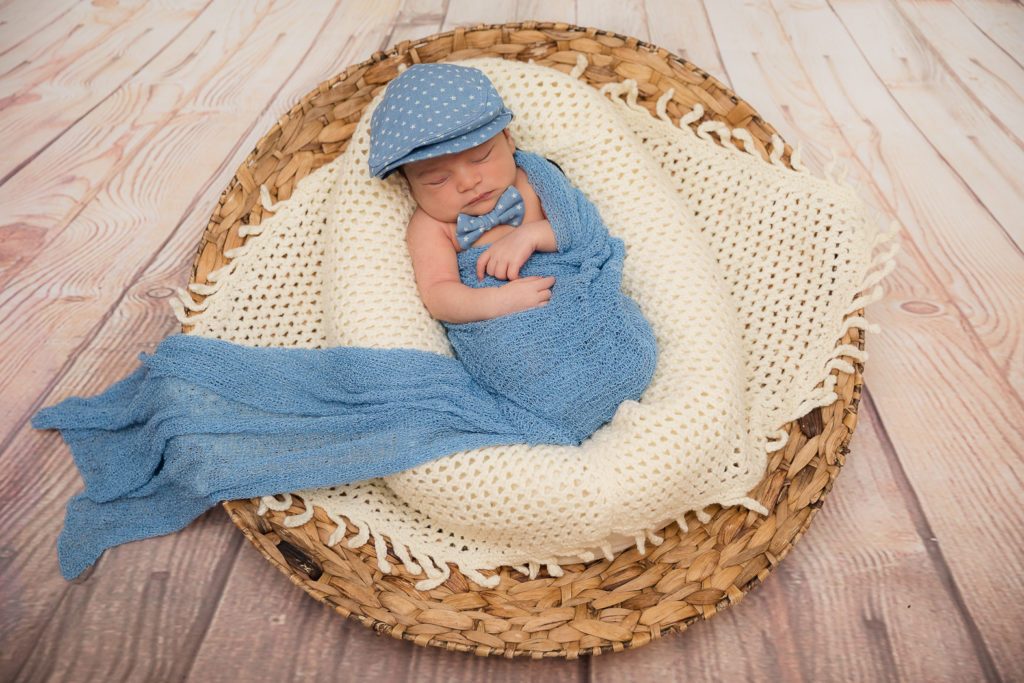 newborn photo with cap and bowtie in a basket